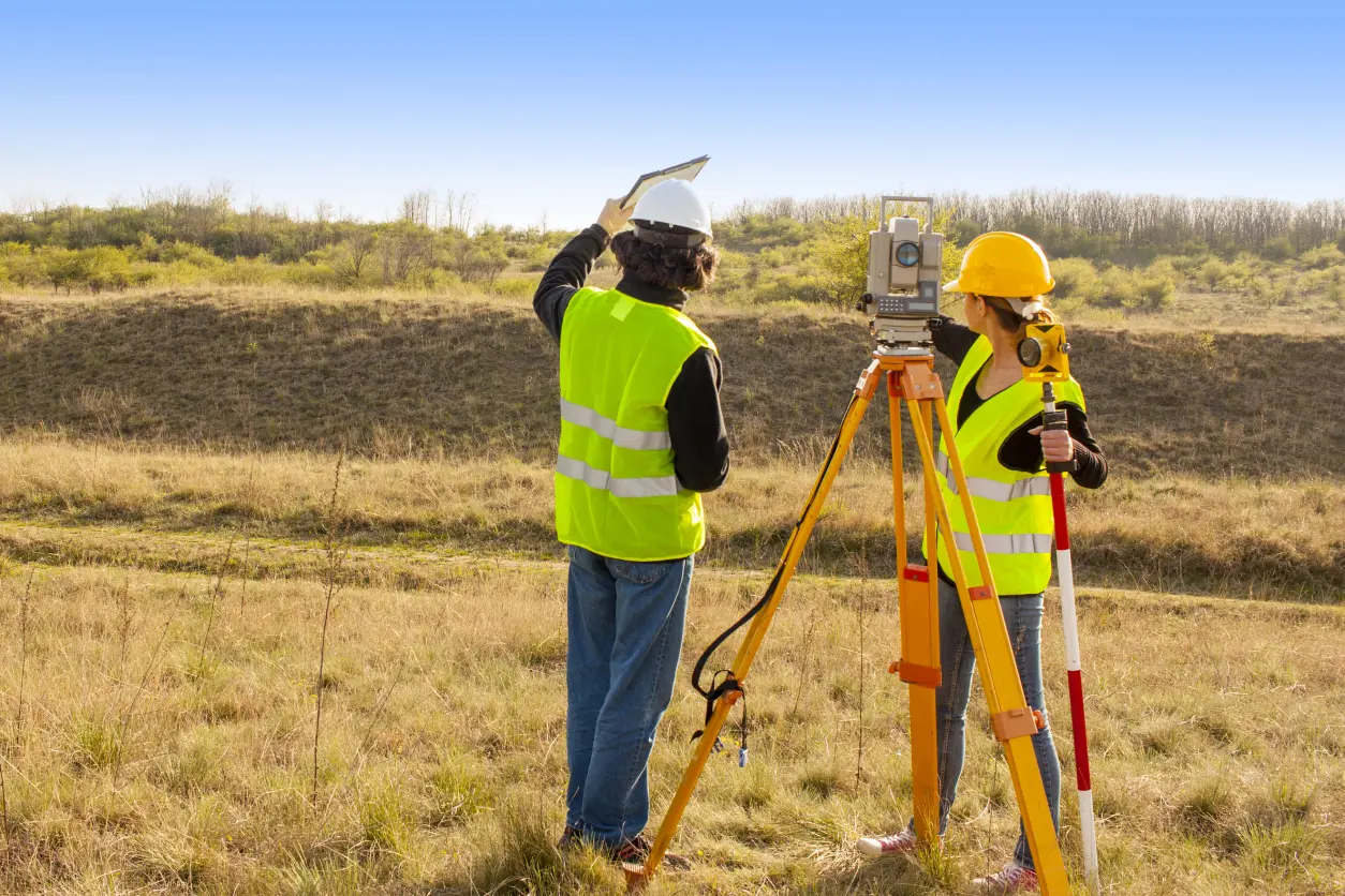 Surveyors working with equipment in grassy field.