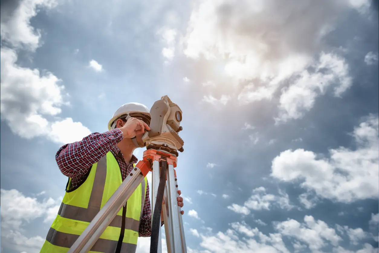 Surveyor using equipment under cloudy sky.