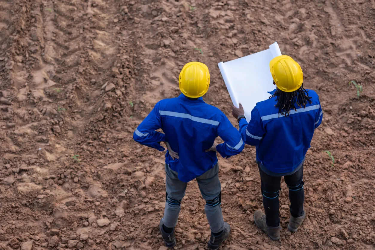Two workers with blueprints on construction site.